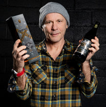 Load the picture into the gallery viewer, Bruce Dickinson holding a Trooper X limited edition anniversary beer bottle and packaging by Robinsons Brewery, 660ml, 10% ABV, celebrating the collaboration with Iron Maiden.
